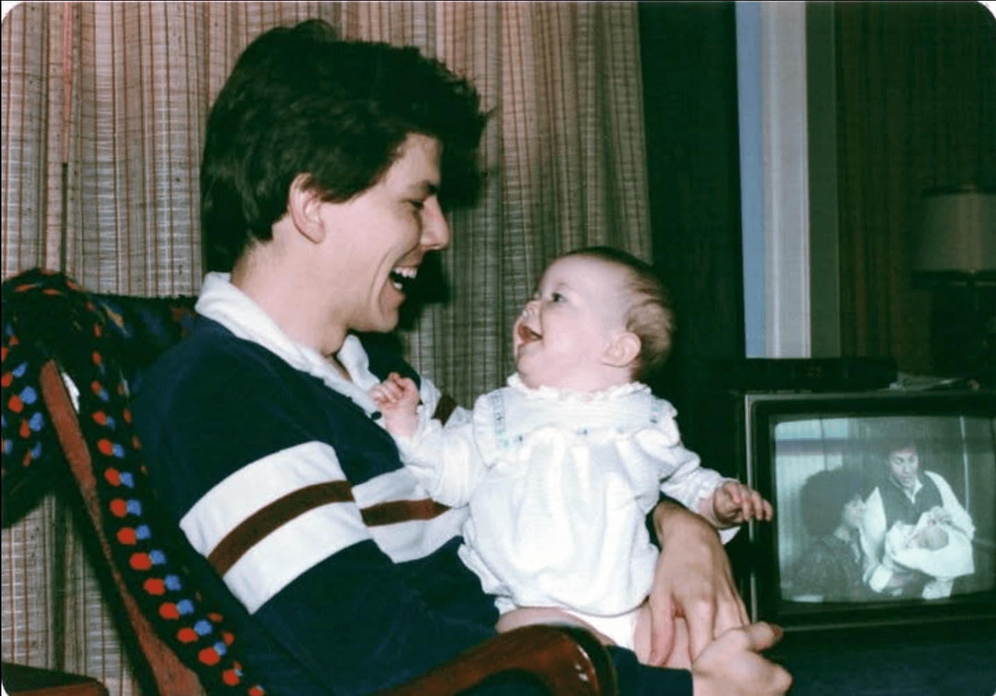 Rachael's dad holding her as a baby, both laughing, the same moment playing on the TV behind them.