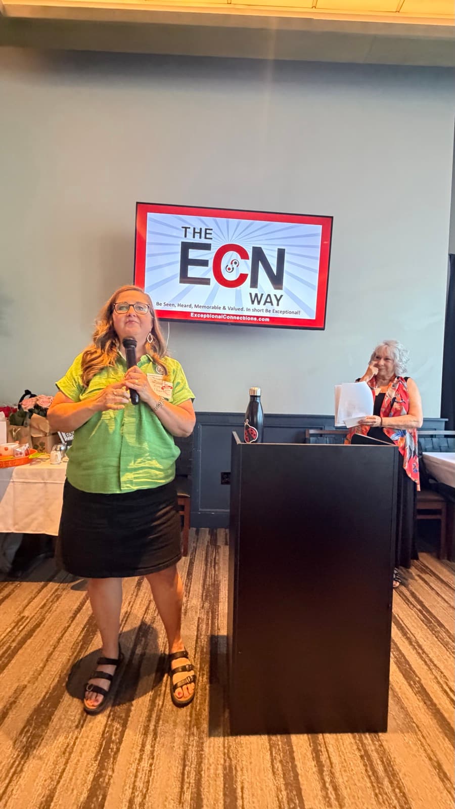 A member speaking during the ECN Way segment at Exceptional Connections, with a screen reading Be Seen, Heard, Memorable and Valued